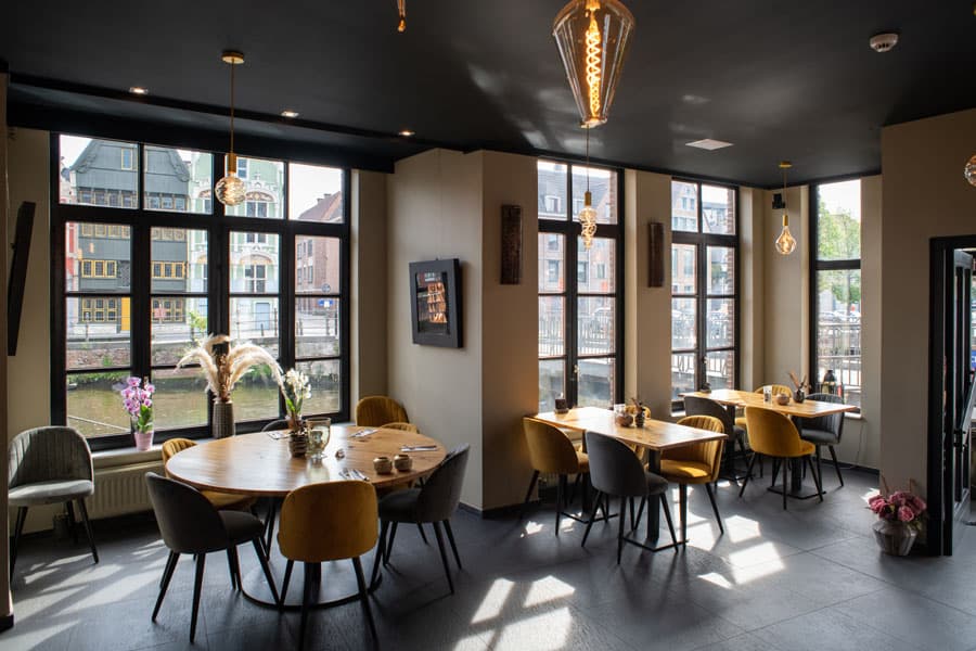 De brasserie binnen, met ronde tafels en grote ramen op de Dijle